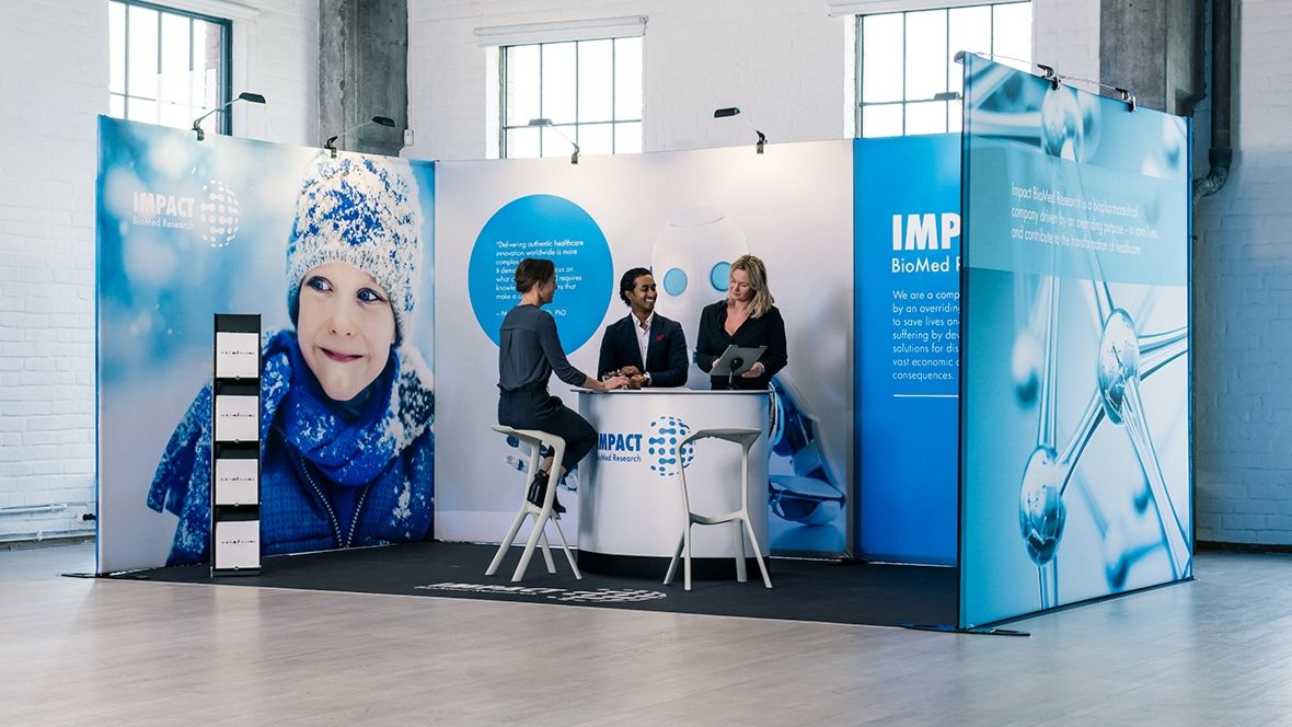 Messestand mit Counter, Prospektständer und großformatigen Bildwänden in heller Industriehalle